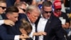 Американскиот републикански кандидат Доналд Трамп со крв на лицето опкружен со агенти на Тајната служба додека го симнуваат од бината на собирот во Батлер, Пенсилванија, на 13 јули 2024 година