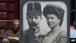 Tourists looking at exhibits in Sarajevo museum, including portraits of Archduke Franz Ferdinand and Sofia von Hochenberg, in Sarejevo, Saturday, June 28, 2014