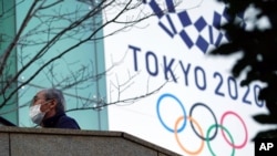 A man wearing a protective mask to help curb the spread of the coronavirus walks near the banner for the Tokyo 2020 Olympic Games Feb. 25, 2021, in Tokyo.