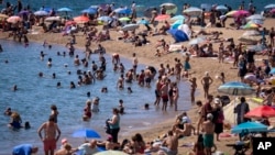 Bañistas se refrescan en el agua mientras otros toman el sol en una playa de Barcelona, España, el 24 de julio de 2024. 