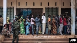 Un soldat rwandais regarde les électeurs faire la queue pour voter au bureau de vote du lycée Barthélemy Boganda dans le 1er district de Bangui, en République centrafricaine, le 27 décembre 2020.