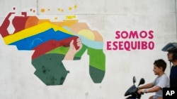 Un niño conduce una motocicleta frente a un mural del mapa venezolano con el territorio Esequibo incluido en el barrio 23 de Enero de Caracas, Venezuela, el lunes 11 de diciembre de 2023.