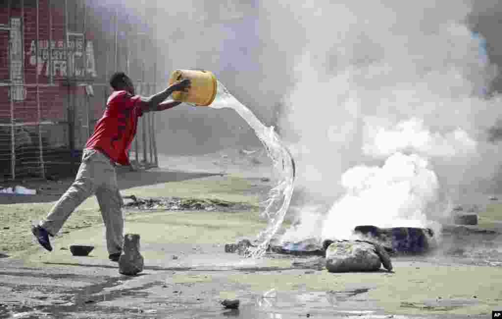 A man throws a bucket of water to put out flames from a tire set on fire in a street by rioting youths, Mombasa, Kenya, Oct. 4, 2013.