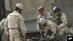 Security force personnel inspect a destroyed car at the scene of a car bomb attack in Baghdad, Iraq, Sunday, May 22, 2011