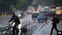 A cyclist and a passer-by with an umbrella cross a traffic light intersection during rainfall in Hamburg, Germany, June 21, 2021.