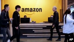 In this Nov. 13, 2018 file photo, employees walk through a lobby at Amazon's headquarters in Seattle. On Friday, May 3, 2019, shares in Amazon are moving higher after billionaire investor Warren Buffett said his firm has been buying the online retailer.