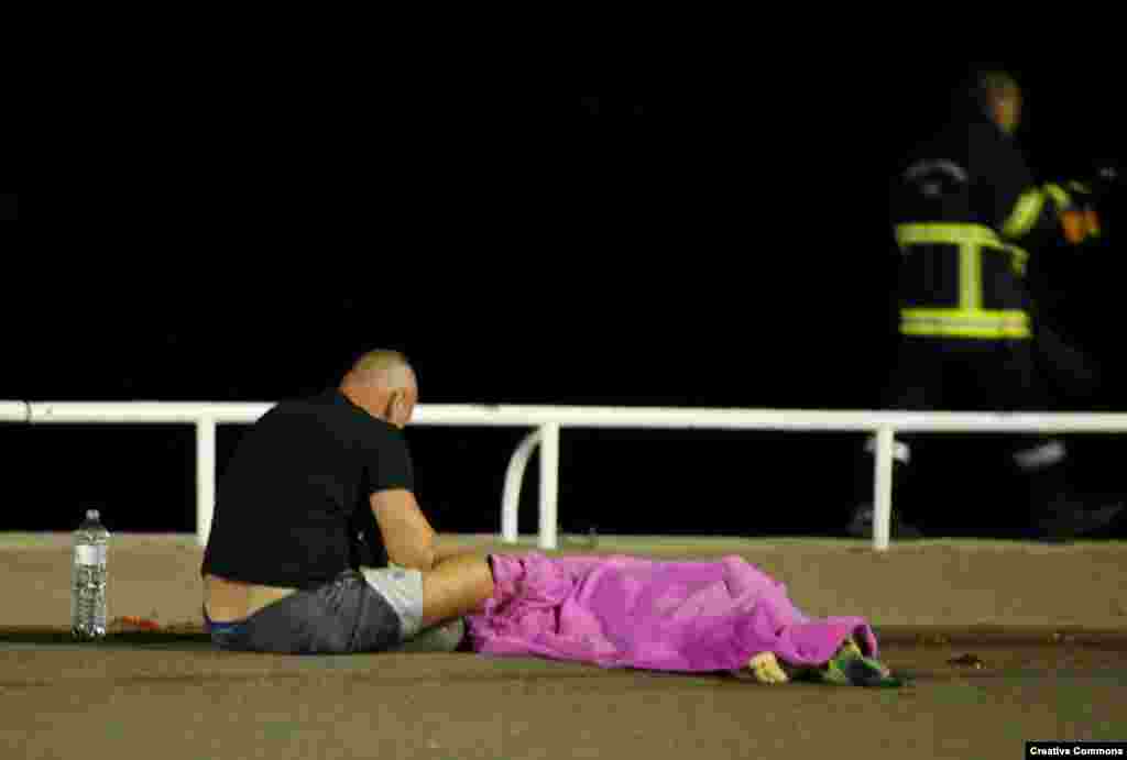 A man sits next to a body seen on the ground July 15, 2016, after a truck ran into a crowd celebrating the Bastille Day national holiday July 14 in Nice, France.