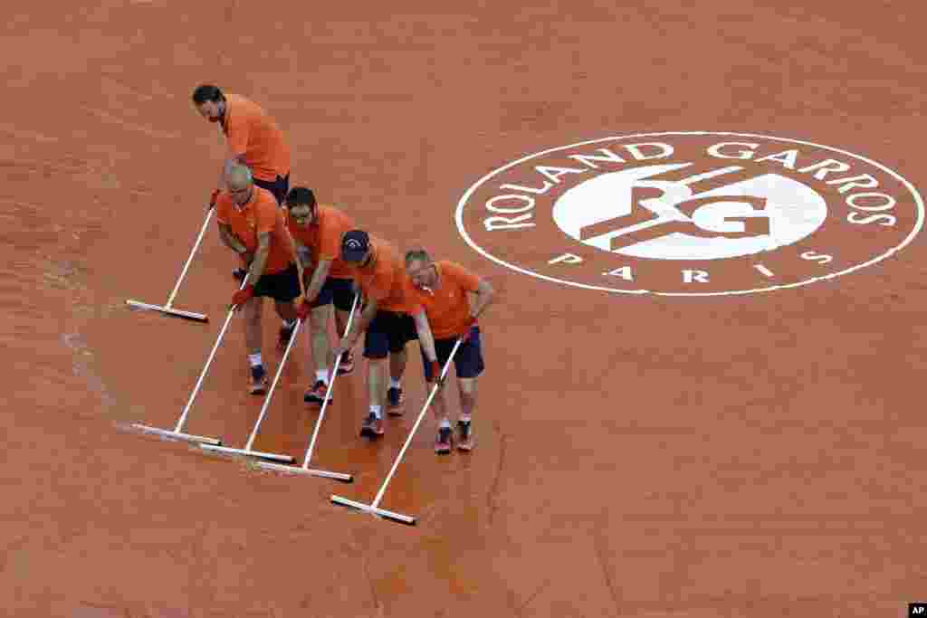 Stadium employees remove water from the court as rain delays the French Open men's quarterfinals at the Roland Garros stadium in Paris, France.