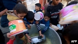 Palestinian children collect food at a donation point provided by a charity group in the southern Gaza Strip city of Rafah, on December 6, 2023, amid continuing battles between Israel and the Palestinian militant group Hamas.