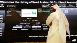 A Saudi stock market official smiles as he watches the stock market screen displaying Saudi Arabia's state-owned oil company Aramco after the debut of Aramco's initial public offering (IPO) on the Riyadh's stock market in Riyadh, Saudi Arabia,…