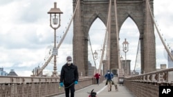 People wear facial masks for protection against the coronavirus as they walk their dogs on the Brooklyn Bridge, Friday, April 10, 2020, in New York. (AP Photo/Mary Altaffer)