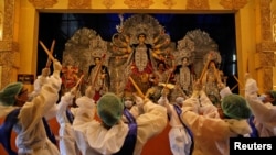 Hindu devotees wearing personal protective equipment perform Dandiya, a traditional dance, in front of an idol of Hindu goddess Durga on the first day of Durga Puja festival in Kolkata, India, Oct. 22, 2020.