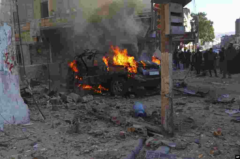 This photo provided by the Syrian Civil Defense White Helmets, which has been authenticated based on its contents and other AP reporting, shows Syrians around a burning car hit by a shell, in the town of Afrin, north of Aleppo. The rocket attack on Afrin, controlled by Turkey-backed opposition fighters, killed several civilians and wounded over a dozen people, Syrian rescuers and a war monitor said.