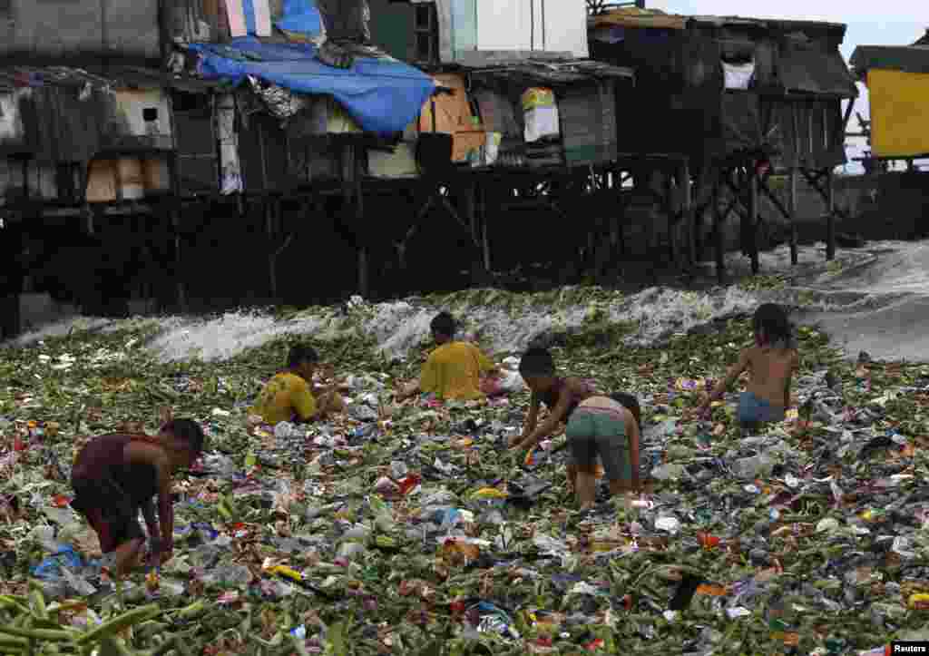 Children sift through floating garbage as they collect recyclable items to sell while strong waves crash along the shores of Manila Bay, near a slum area in Manila, Philippines.