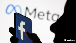 Seorang perempuan memegang smartphone dengan logo Facebook di depan tampilan logo baru Facebook rebrand Meta dalam gambar ilustrasi ini diambil 28 Oktober 2021. (Foto: Reuters)