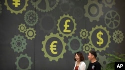 People walk past a mural on a bank showing symbols for American, Chinese and other world currencies in Beijing, July 7, 2018.