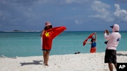 FILE - Chinese tourists take souvenir photos with the Chinese national flag as they visit Quanfu Island, one of Paracel Islands of Sansha prefecture of southern China's Hainan province in the South China Sea, Sept. 14, 2014. 