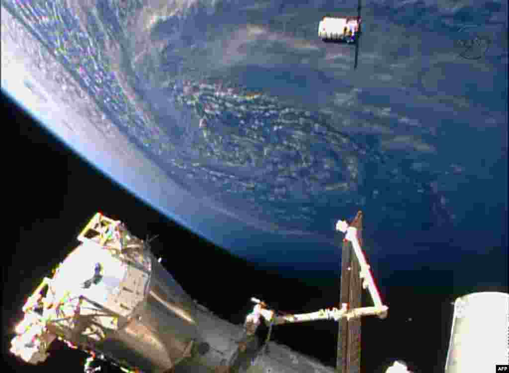 Sebuah potret yang diambil dari TV NASA menunjukkan pesawat kargo antariksa tanpa awak 'Cygnus' (atas) tiba di stasiun antariksa internasional (ISS) dengan Bumi tampak di latar belakangnya.