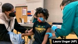 Cadell Walker (à g.) réconforte sa fille Solome, 9 ans, pendant que l'infirmière Cindy Haskins lui administre le vaccin de Pfizer le samedi 13 novembre 2021 à Louisville, dans le Kentucky.