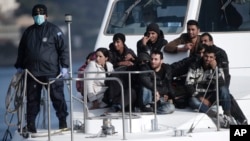 A Greek coast guard officer, wearing a mask for fear of infectious disease, stands next to a small group of immigrants on a launch carrying them to shore from a crippled ship holding more than 700 people at the coastal Cretan port of Ierapetra, Greece, No