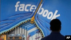 FILE - A Facebook employee walks past a sign at Facebook headquarters in Menlo Park, California, March 15, 2013. 