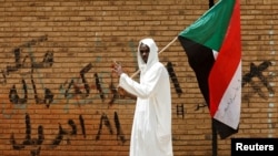 FILE - A protester makes a victory sign as he carries a Sudanese flag in front of the Defense Ministry in Khartoum, Sudan, April 19, 2019. 