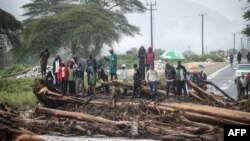 People stand on debris blocking a highway after River Muruny burst its bank following heavy rains in Parua village, about 85 km northeast of Kitale, in West Pokot county, western Kenya, Nov. 24, 2019.