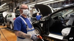 Un empleado se encuentra cerca de vehículos en producción con una máscara facial en la planta de VW en Wolfsburg, Alemania. Volkswagen está lanzando gradualmente la producción en plantas importantes después del cierre de la corona. 