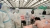 Para petugas kesehatan dengan pakaian hazmat memeriksa kondisi pasien anak yang terjangkit COVID-19 yang dirawat di Shanghai New International Exhibition Hall pada 9 April 2022. Gedung Ekshibisi itu kini telah diubah menjadi rumah sakit darurat. (Foto: China Daily via Reuters)