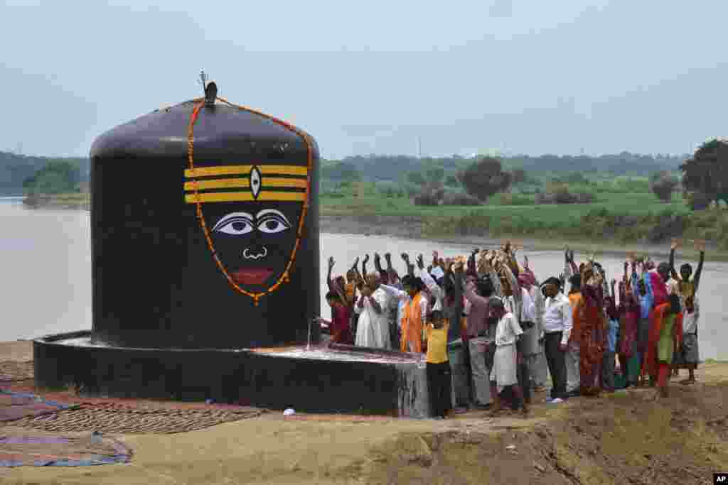 Para pemuja dewa Hindu Siwa mengangkat tangan mereka sambil melantunkan nyanyian relijius saat menyembah 'lingam', yang baru selesai dipasang di tepi sungai Yamuna di Agra, India. (AP Photo/Pawan Sharma)