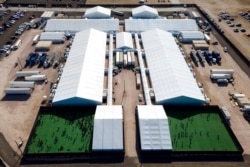 FILE - Migrants are seen in a green area outside of a soft-sided detention center after they were taken into custody while trying to sneak into the U.S., in Donna, Texas, March 19, 2021.