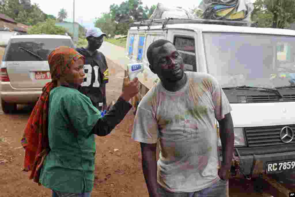 A health worker uses a thermometer to screen a man's temperature at a makeshift road block run by Guinean security forces near the town of Forecariah, Guinea, Sept. 7, 2014. 