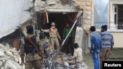A civil defense member gestures towards a rebel fighter as they search for survivors at a site hit by what activists said were airstrikes carried out by the Russian Air Force in Idlib city, Syria Dec. 20, 2015.