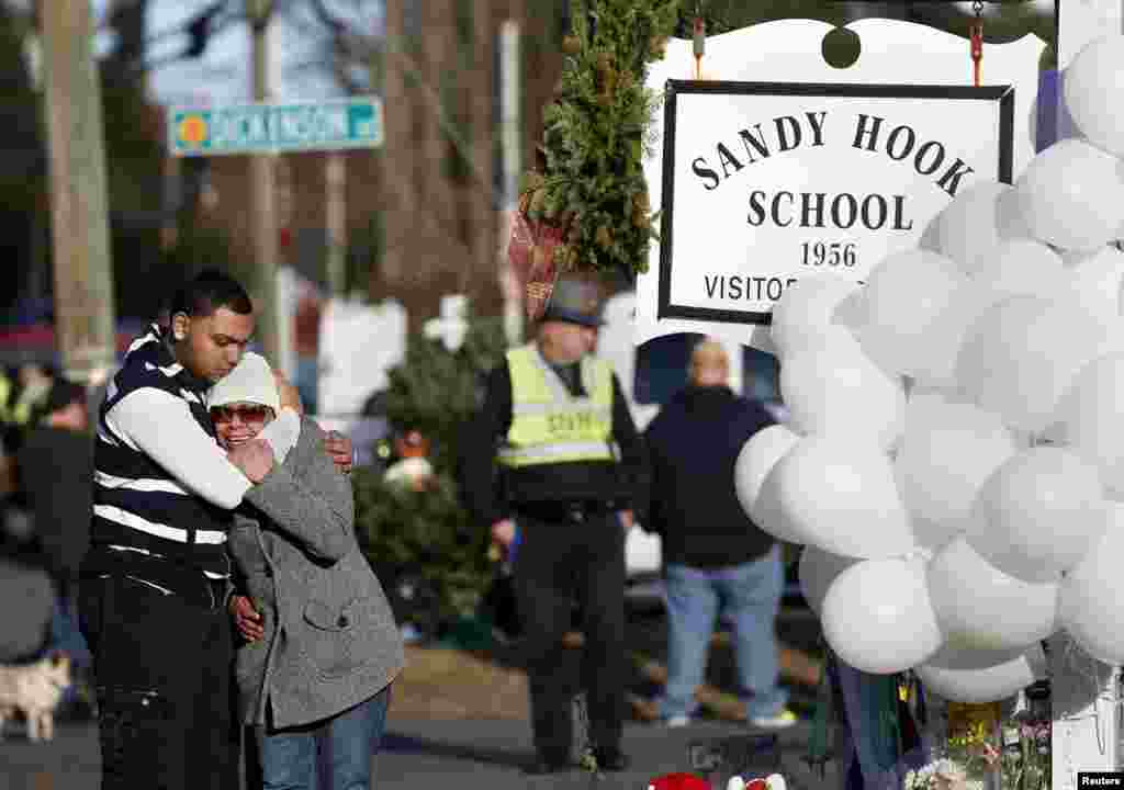 Warga mengungkapkan dukacitanya di dekat tumpukan balon-balon dan bunga-bunga yang diletakkan di dekat SD Sandy Hook di Newtown, Connecticut untuk mengenang para korban penembakan di sekolah itu, 15 Desember 2012.