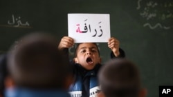 A Syrian refugee boy holds up a placard in Arabic, during class at a remedial education center run by Relief International in the Zaatari Refugee Camp, near Mafraq, Jordan, Jan. 21, 2016.