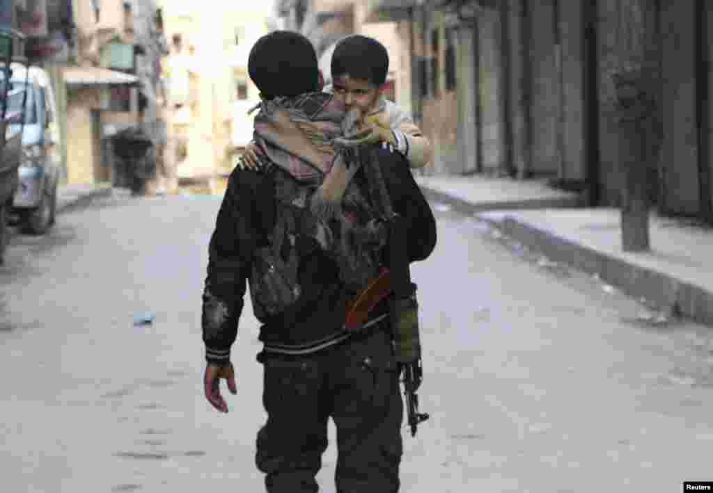 A Kurdish fighter from the Popular Protection Units (YPG) carries his son as he walks along a street, Sheikh Maqsoud neighborhood, Aleppo, Feb. 18, 2014. 