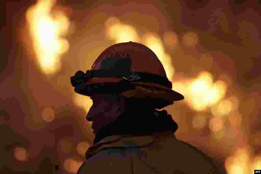 Seorang petugas pemadam kebakaran memantau kebakaran"Colby Fire" pada hari kedua di lereng bukit di atas Jalan Bebas Hambatan 39 di Azusa, California. Tiga orang telah ditangkap dengan tuntutan mengobarkan api tersebut yang sekarang telah membakar 1.700 hektar lahan dan beberapa rumah di San Gabriel Valley.