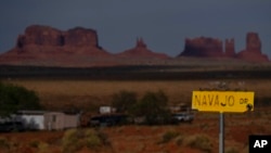 FILE - In this April 30, 2020, photo, a sign marks Navajo Drive as Sentinel Mesa, homes and other structures in Oljato-Monument Valley, Utah on the Navajo Reservation, stand in the distance. 
