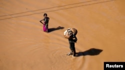 A girl stops to look as a man walks past carrying luggage on his head after Cyclone Idai in Buzi district outside Beira, Mozambique, March 22, 2019.