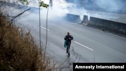 A pedestrian takes cover from clouds of tear gas fired by the Bolivarian National Police during clashes at an anti-government protest in Caracas, Venezuela, March 20, 2014. 