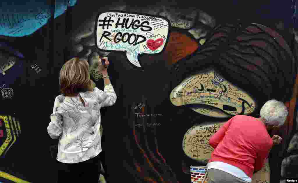 Tourists write messages on a section of the Peace Wall in the loyalist Shankill area of West Belfast in Northern Ireland. Britain and Ireland sought to calm Northern Ireland's political crisis on Friday by urging Protestant unionists and Catholic nationalists to preserve a power-sharing government that ended decades of sectarian violence.