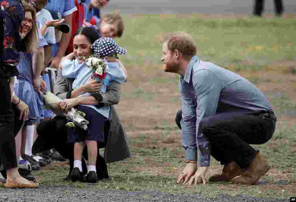 Britain's Prince Harry looks on as his wife Meghan, Duchess of Sussex, is hugged by Luke Vincent, 5, on their arrival in Dubbo, Australia.