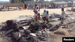 FILE - People stand amid the damage at a camp for displaced people after an attack by suspected members of the Islamist Boko Haram insurgency in Dalori, Nigeria, Nov. 1, 2018. 
