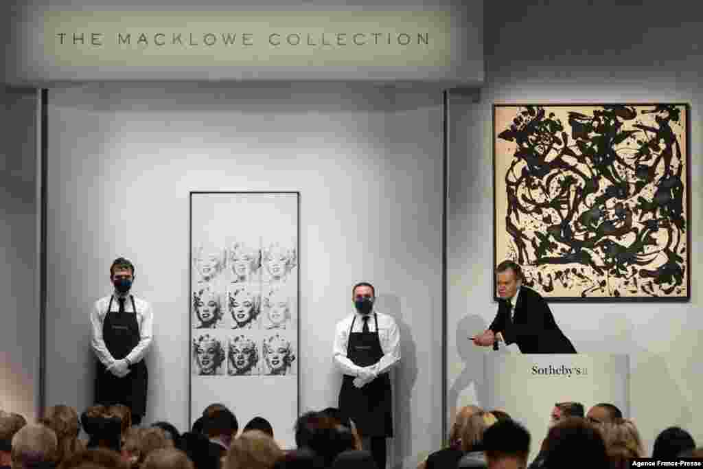 Sotheby's auctioneer Oliver Barker leads an auction of The Macklowe Collection, alongside Andy Warhol's "Nine Marilyns" (L), which sold for $47,373,000, and Jackson Pollock's "Number 17, 1951" (R), at Sotheby's in New York, Nov. 15, 2021.