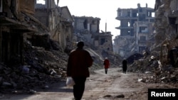 FILE - People walk past damaged buildings at the Yarmouk Palestinian refugee camp on the southern outskirts of Damascus, Syria, Dec. 2, 2020. 
