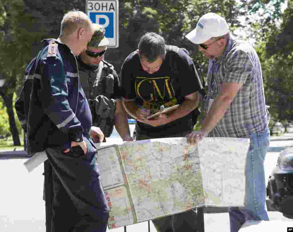 Ukrainian emergencies ministry officer, left, Donetsk People's Republic fighter, 2nd left, and members of the OSCE mission in Ukraine examine a map as they discuss the situation around the site of crashed Malaysia Airlines MH17, in the city of Donetsk, July 27, 2014.