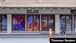 Seorang wanita berjalan melewati tanda "Stay Safe Melbourne" pada hari pertama penguncian COVID-19 selama tujuh hari di Melbourne. (Foto: Reuters)