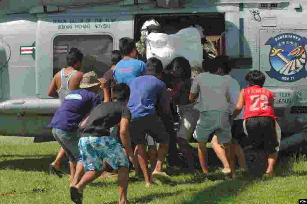 Residents of Lawaan rush to offload food being brought in by a U.S. Navy helicopter, Philippines, Nov. 19, 2013. (Steve Herman/VOA)