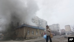 Seorang perempuan melewati rumah yang terbakar akibat serangan roket di Mariupol, Ukraina timur (24/1). (AP/Sergey Vaganov)
