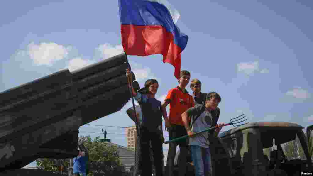 Children holding a Russian flag pose for photos on a destroyed Ukrainian army Grad multiple rocket launcher system that was seized and put on public display at the central square in Donetsk, Ukraine, Aug. 24, 2014.